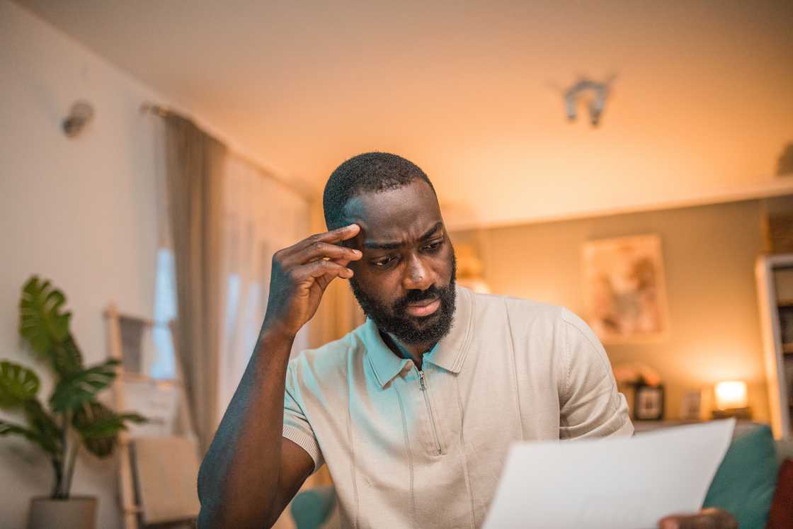 A man staring at a document while sitting on the sofa