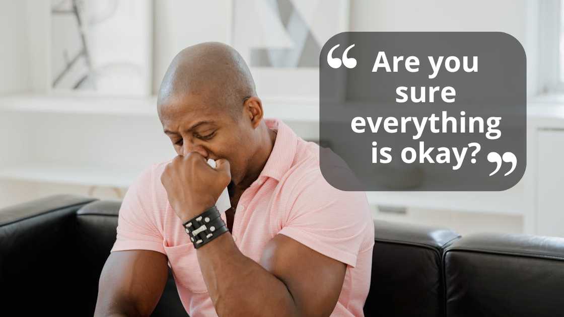 A man sits on a couch with his hand over his mouth, appearing upset. A man sits on a couch with his hand over his mouth, appearing upset.