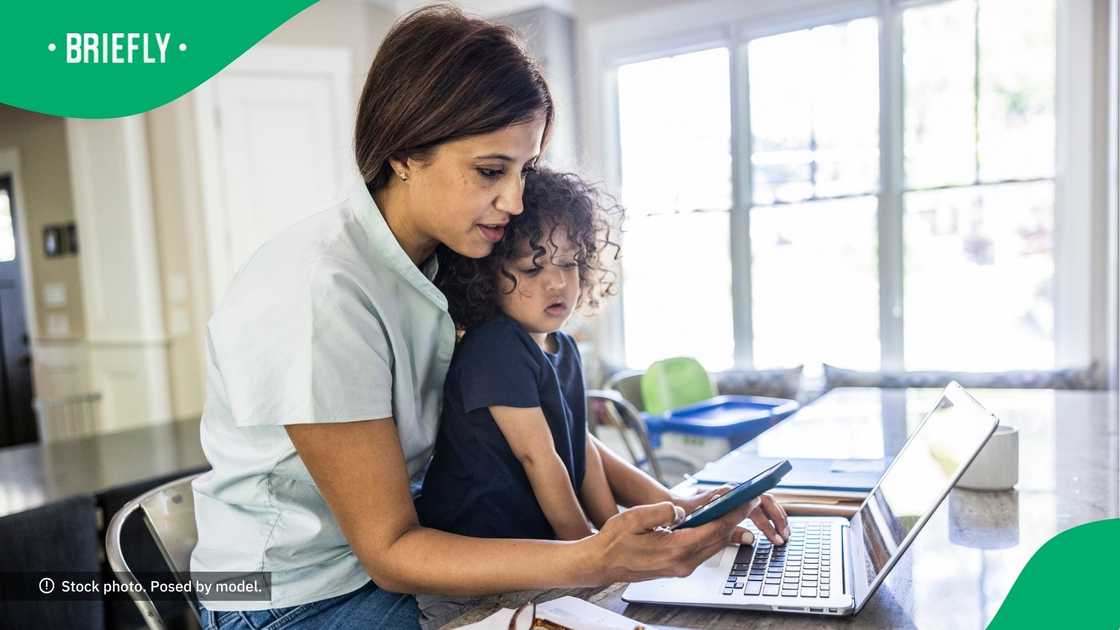 A mother working from home while holding her toddler.