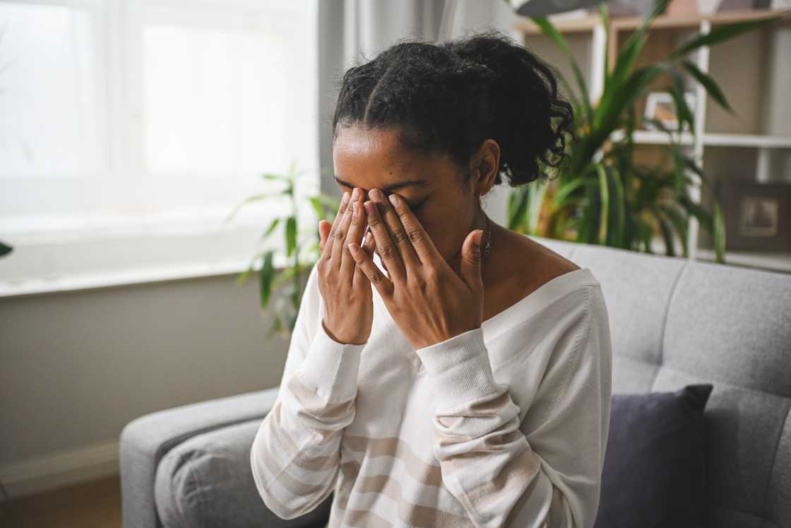 A distraught black woman is sitting on a sofa
