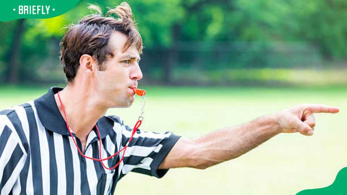 Caucasian referee points as he blows his whistle