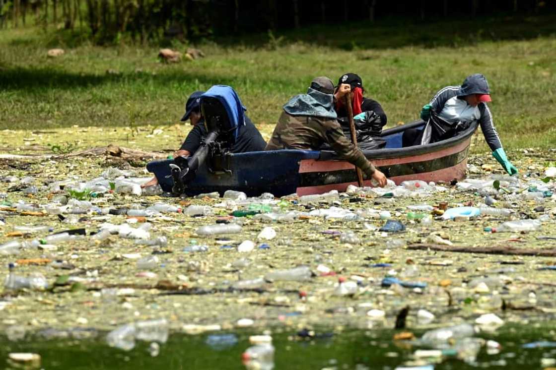 People in a boat clean up plastic rubbish from the Cerron Grande in Potonico, El Salvador by hand People in a boat clean up plastic rubbish from the Cerron Grande in Potonico, El Salvador by hand
