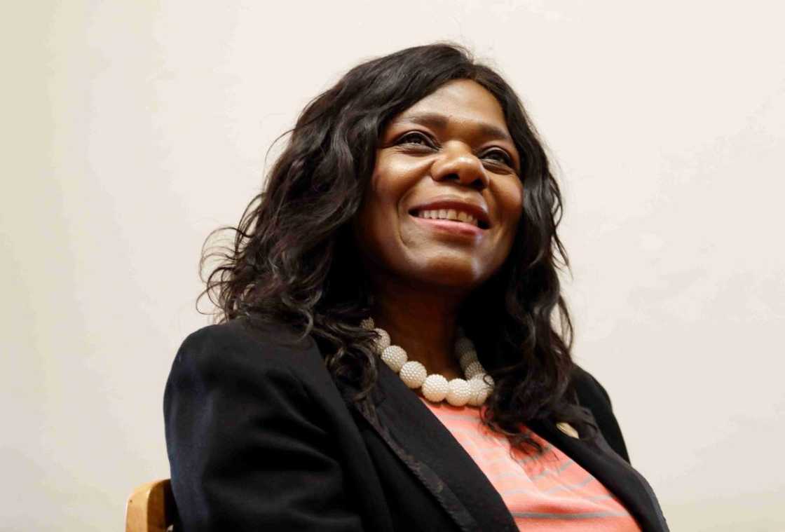 Thuli Madonsela seated at an event in a black coat, pink dress and white pearls. Thuli Madonsela seated at an event in a black coat, pink dress and white pearls.