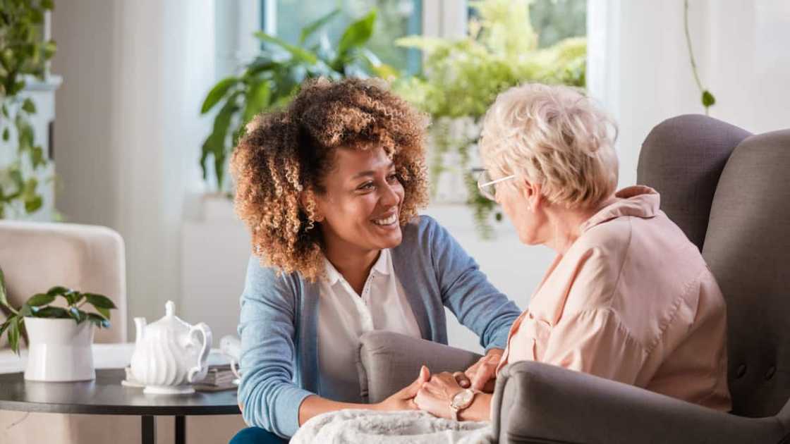 Female home caregiver talking with senior woman, sitting in living room and listening to her carefully Female home caregiver talking with senior woman, sitting in living room and listening to her carefully