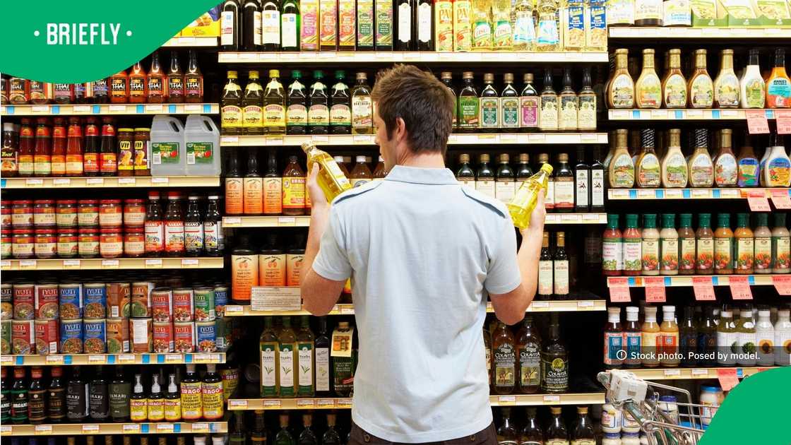 A young man in supermarket comparing bottles of oil
