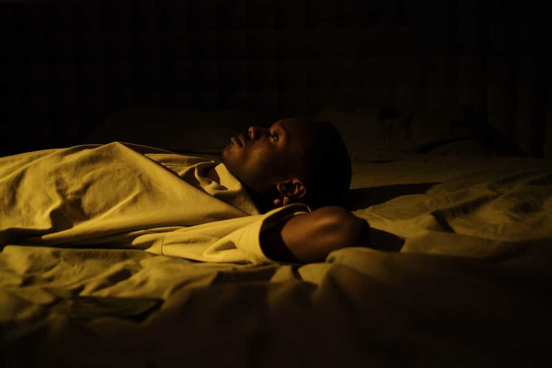 A man lying awake on a bed at night under dim light. A man lying awake on a bed at night under dim light.
