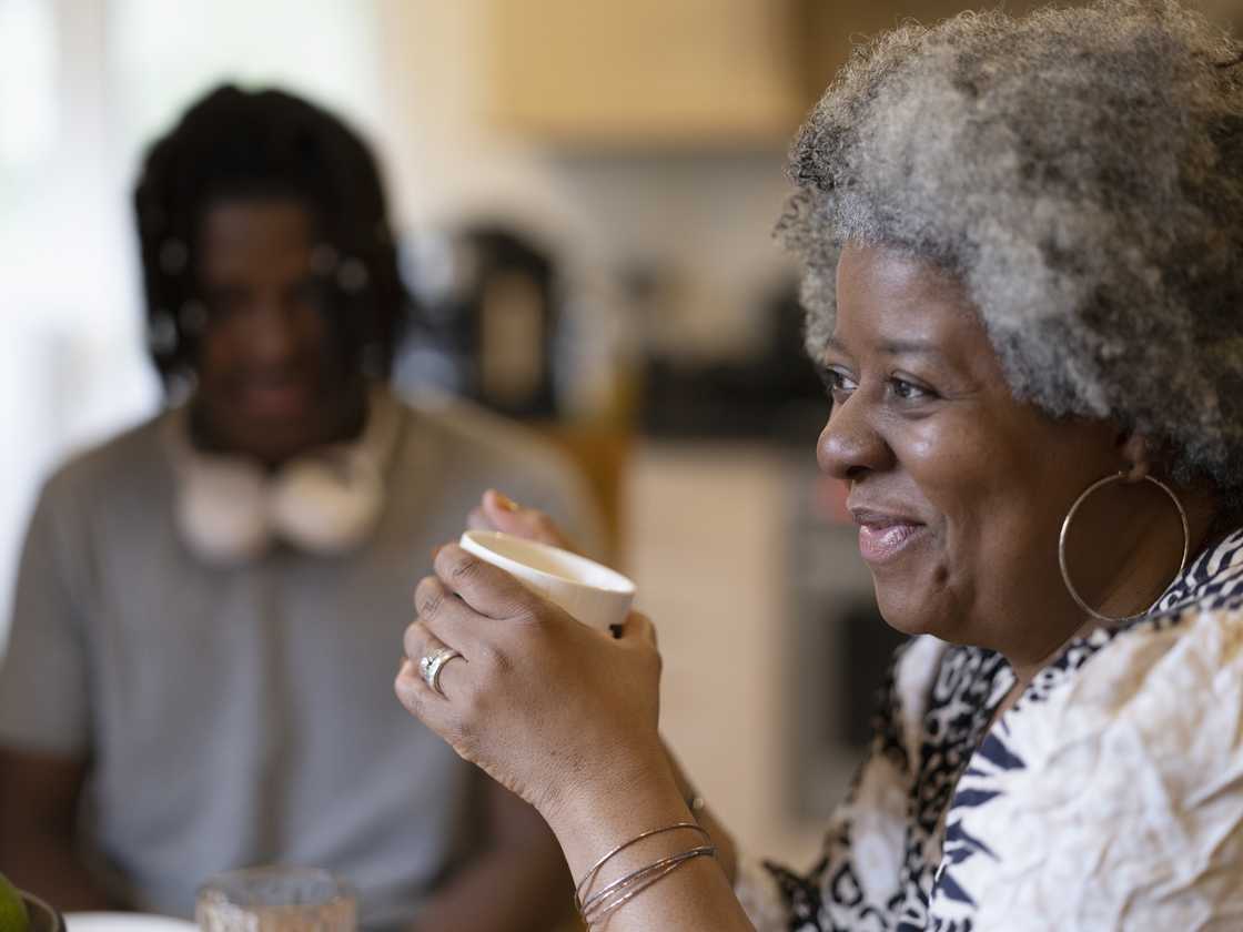 An elderly woman and a young man have coffee.