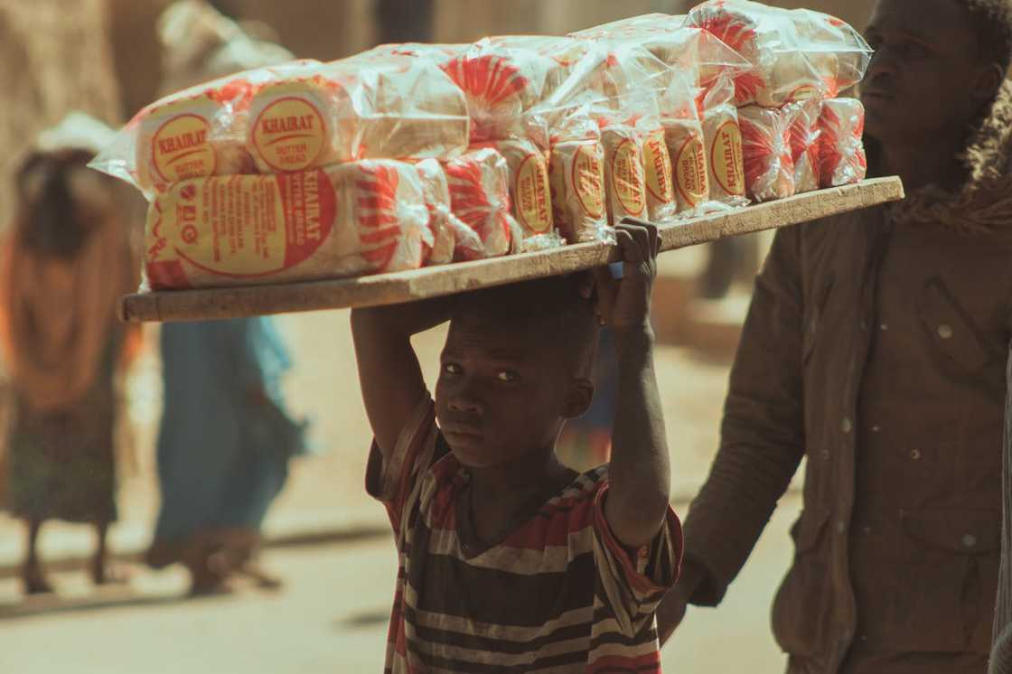 A boy carrying a tray of packaged bread on his head. A boy carrying a tray of packaged bread on his head.