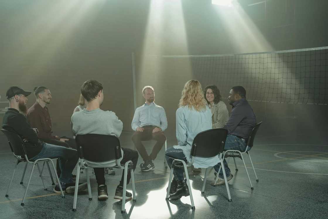 A group of people sitting on chairs in a circle inside a room A group of people sitting on chairs in a circle inside a room