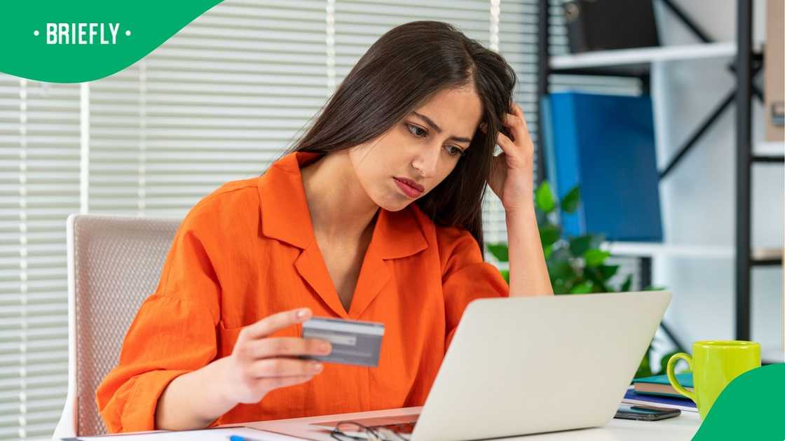 A stock photo of a woman staring at her laptop while holding a credit card A stock photo of a woman staring at her laptop while holding a credit card
