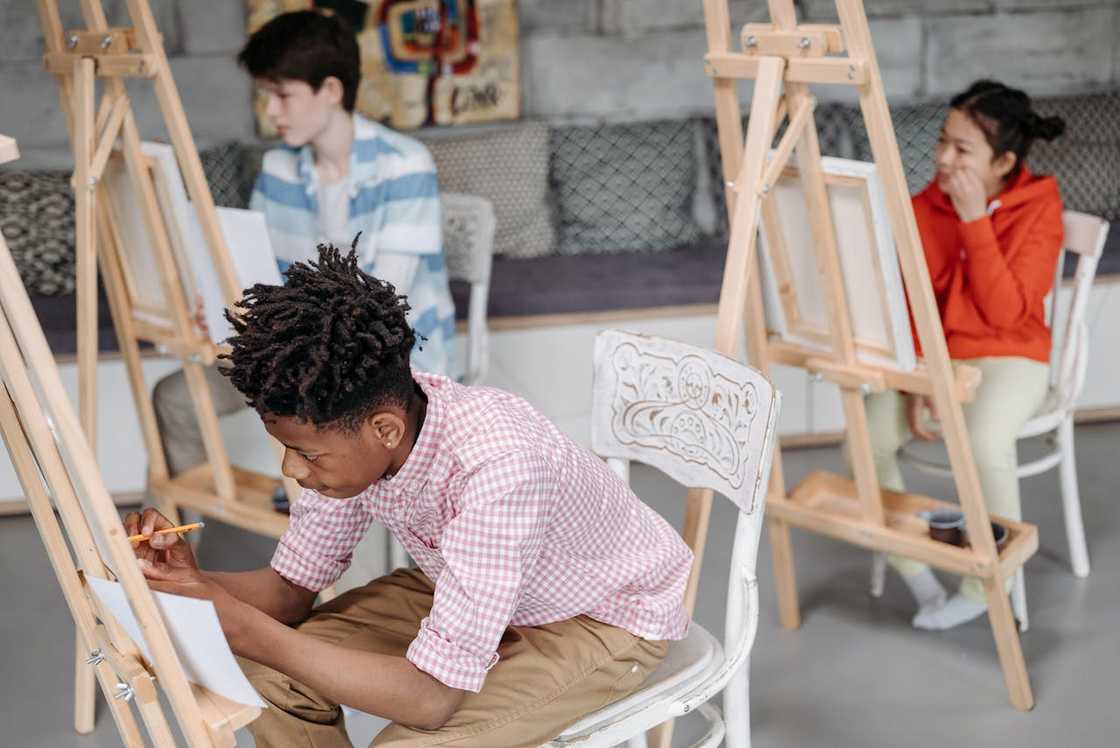 Students sit at easels, drawing in an art class. Students sit at easels, drawing in an art class.