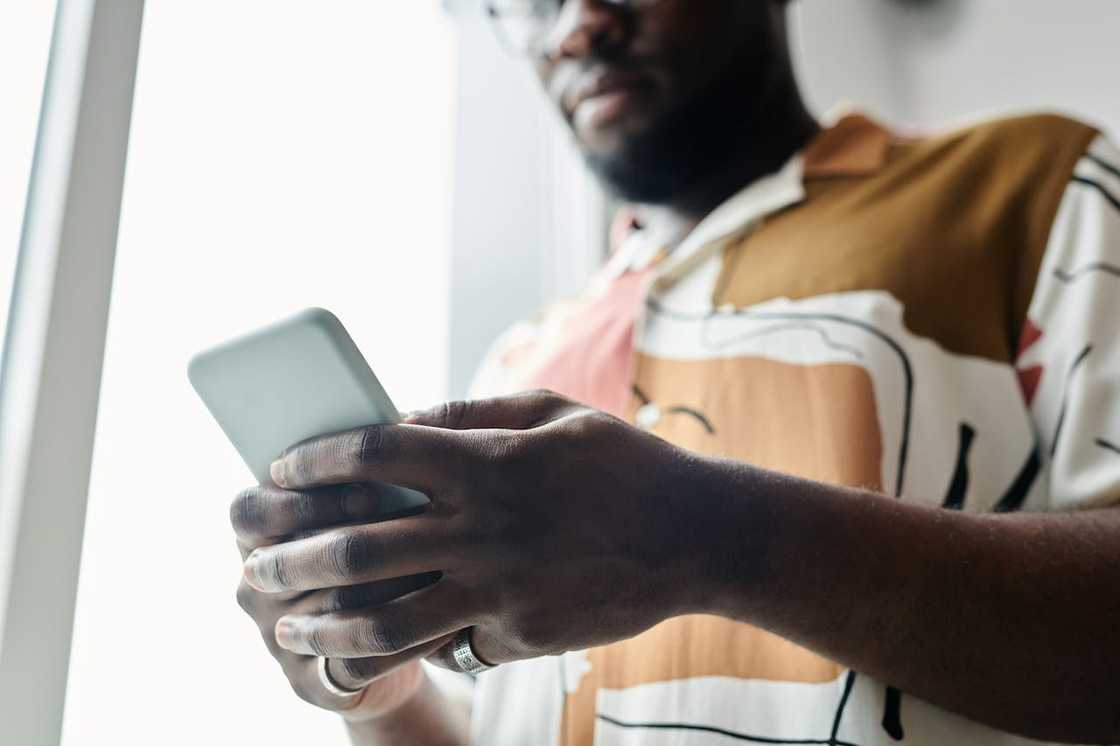 A man holds a smartphone near a window. A man holds a smartphone near a window.
