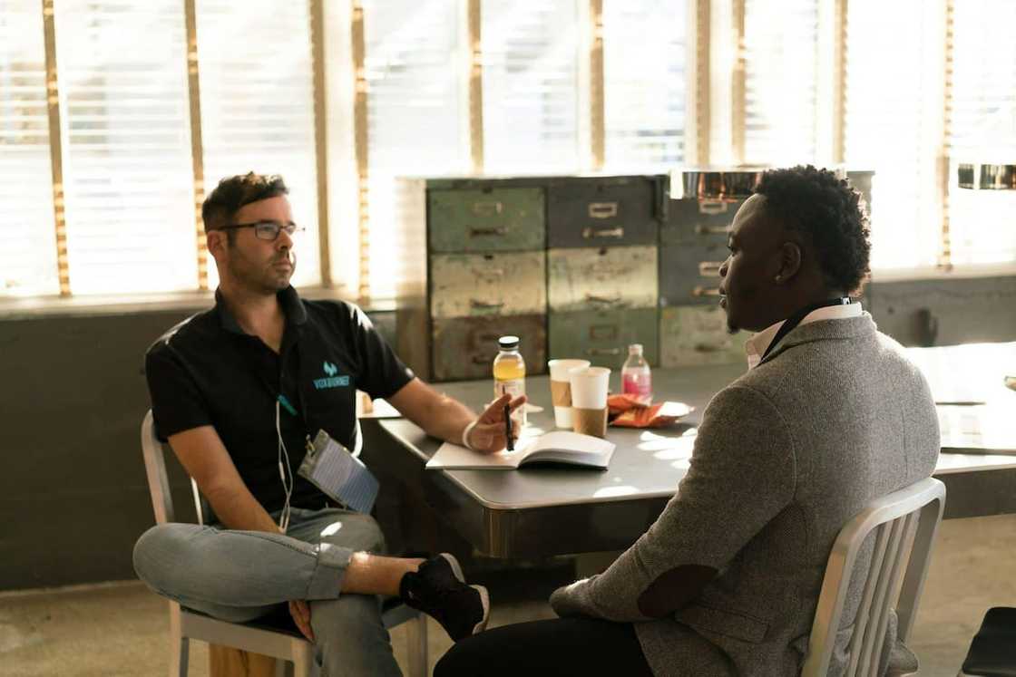 Two men having a discussion while sitting at a desk with a pen and notebook Two men having a discussion while sitting at a desk with a pen and notebook
