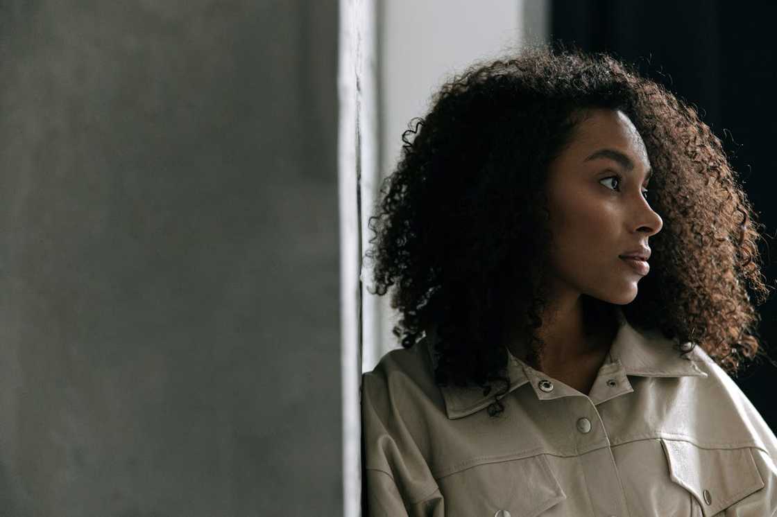 Woman standing by a wall, looking thoughtfully to the side.