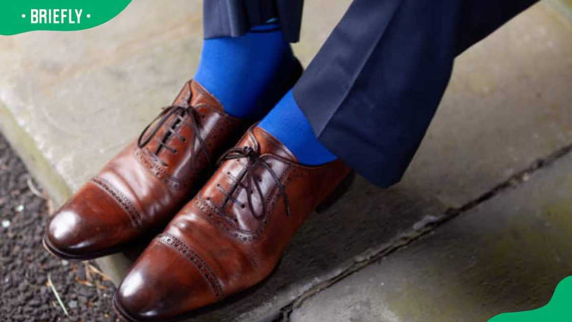 A man wearing luxurious brown leather shoes and vibrant blue socks