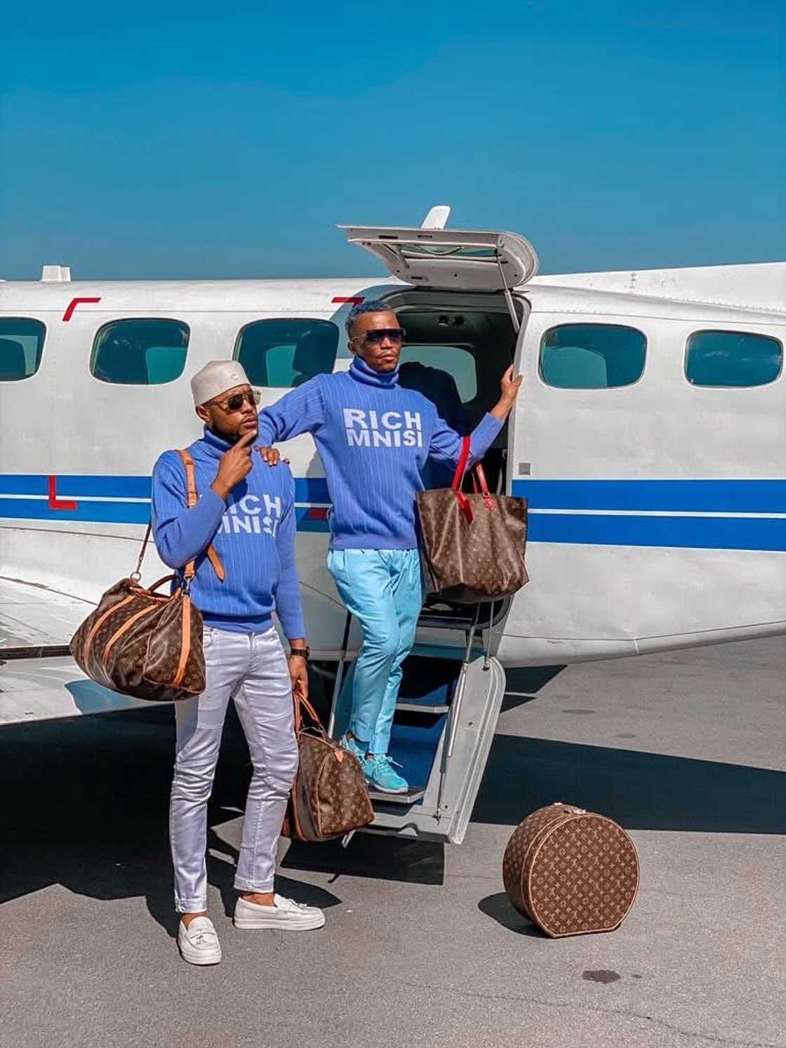 Somizi and Mohale wearing the same jersey infront of a plane
