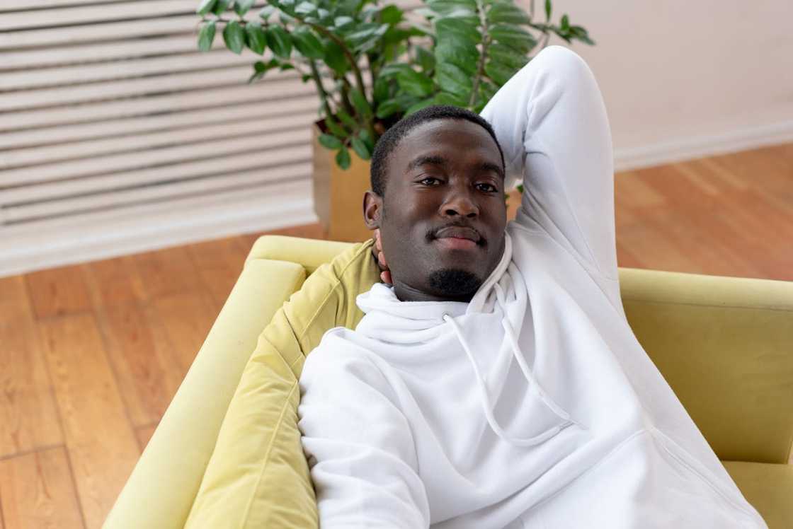 A man in a white hoodie relaxes on a sofa with his arm behind his head. A man in a white hoodie relaxes on a sofa with his arm behind his head.