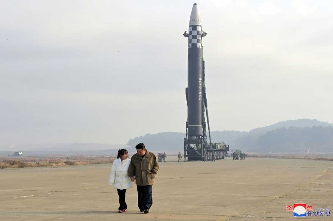 KCNA photos show Kim holding hands with a girl in a white jacket and red shoes, walking in front of a giant missile