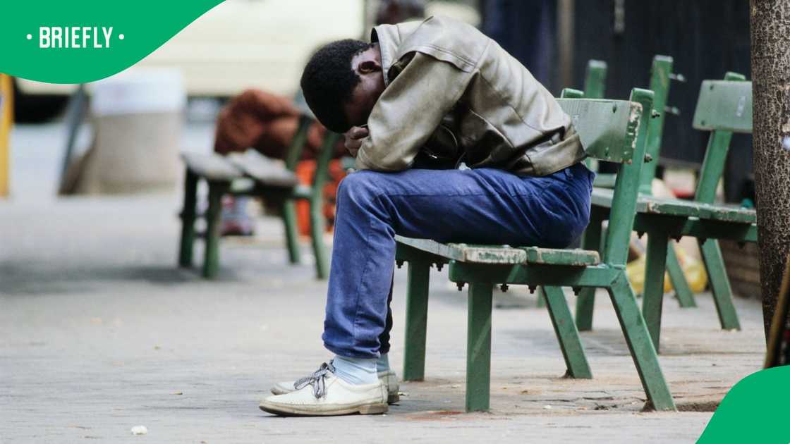 Unemployed black South African man sitting on a bench, with his head in his hands, in Johannesburg, South Africa