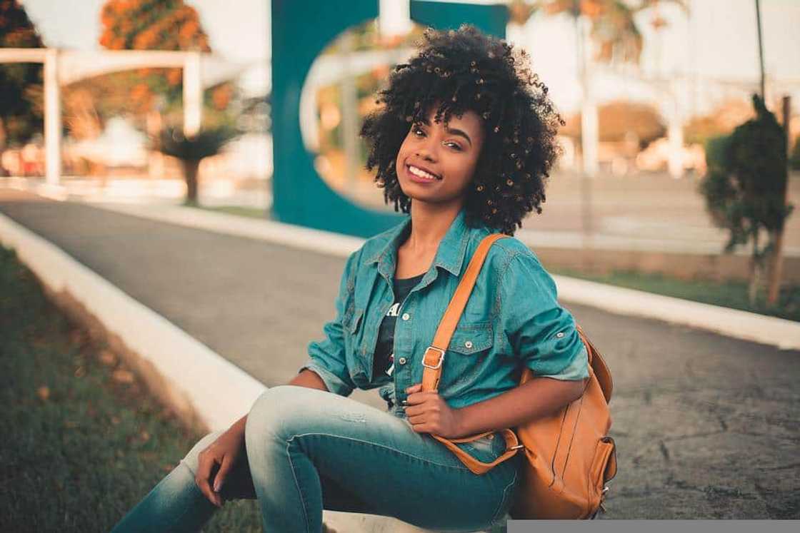 A young female student in denim and a brown bag is sitting down by the pavement kerb A young female student in denim and a brown bag is sitting down by the pavement kerb