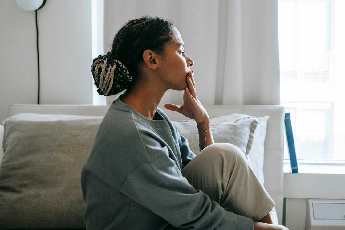 A woman sits on a couch with her hand over her mouth, staring ahead in thought.