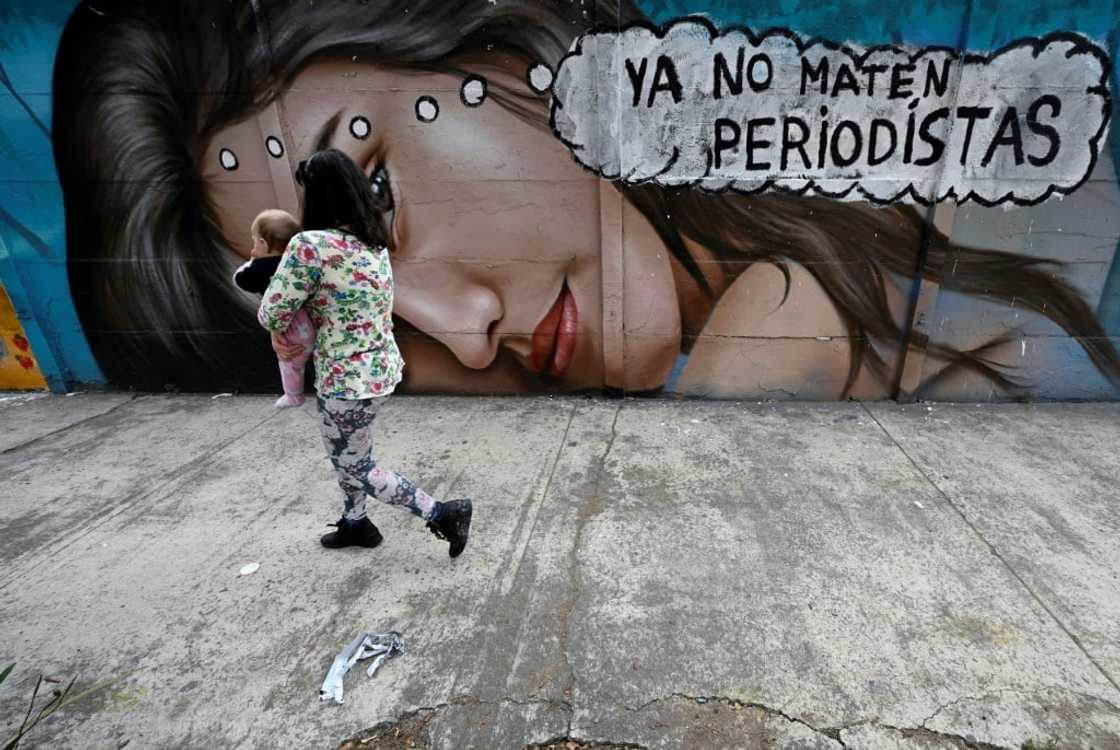 A woman holding a baby walks past a mural reading 'Stop killing journalists' in Mexico City