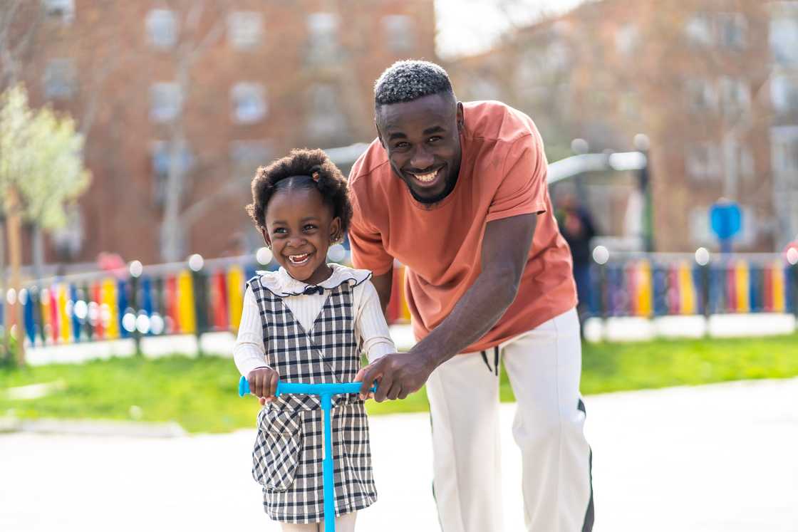 A girl riding a scooter with her father.