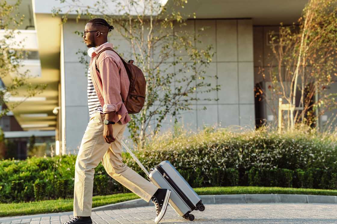A Young African-American man in casual clothing with a suitcase and backpack A Young African-American man in casual clothing with a suitcase and backpack
