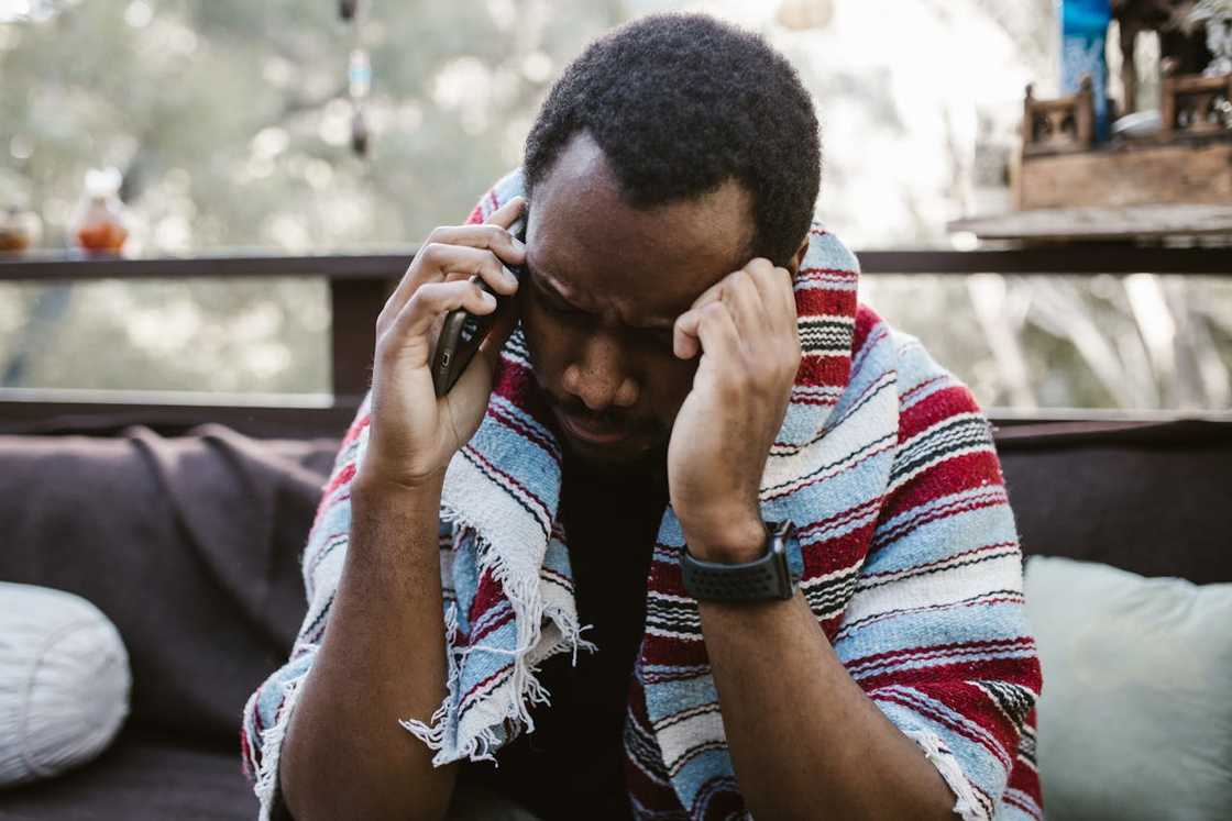 A man on a phone call with his head bowed, appearing stressed. A man on a phone call with his head bowed, appearing stressed.