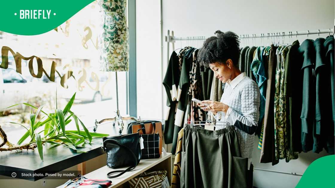 A woman in a clothing store smiling at her phone. A woman in a clothing store smiling at her phone.