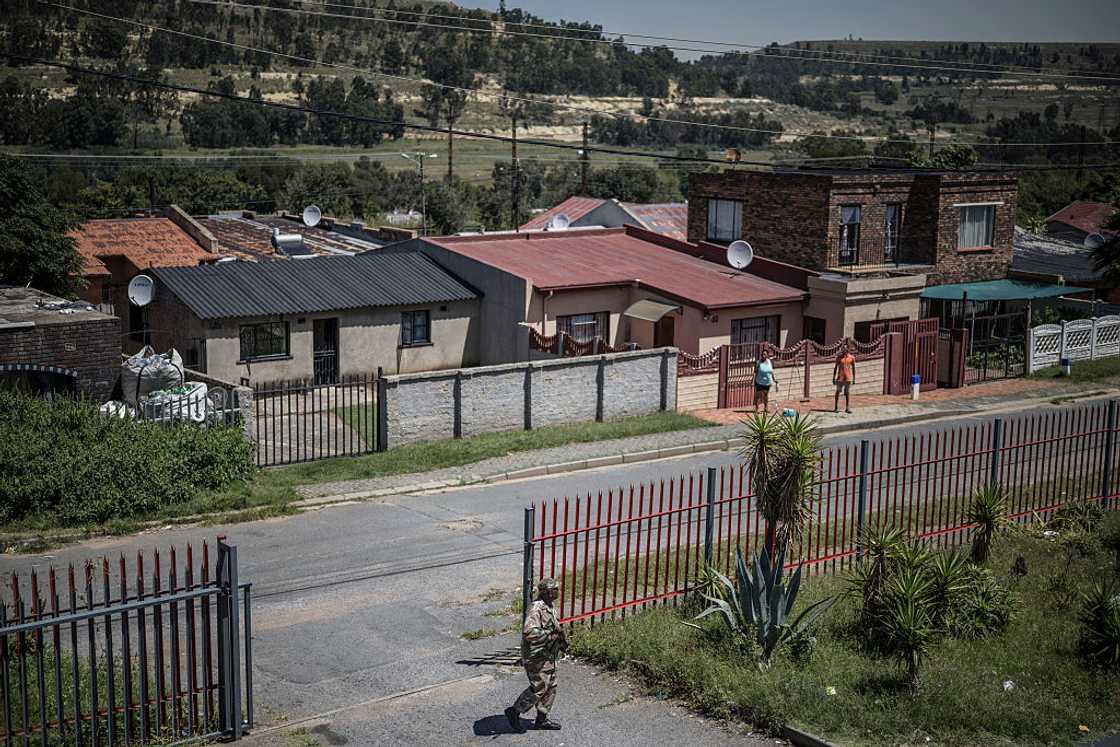 A South African National Defence Force (SANDF) soldier patrols as unseen South Africa Police Service (SAPS) officers conduct a house search in Westbury, Johannesburg, on March 11, 2026