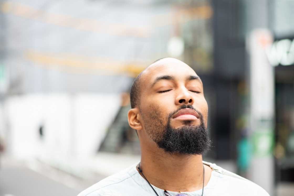 A man standing outside with his eyes closed enjoying a moment of peace.
