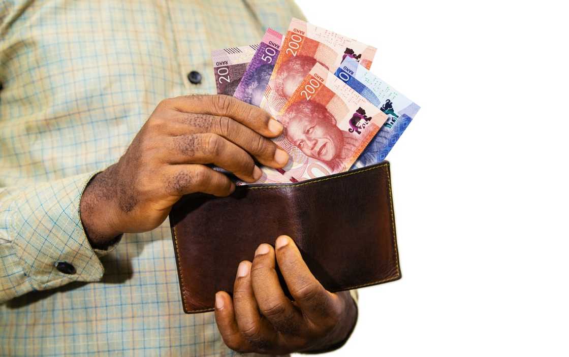 A black person holding a brown wallet with South African Rand notes A black person holding a brown wallet with South African Rand notes