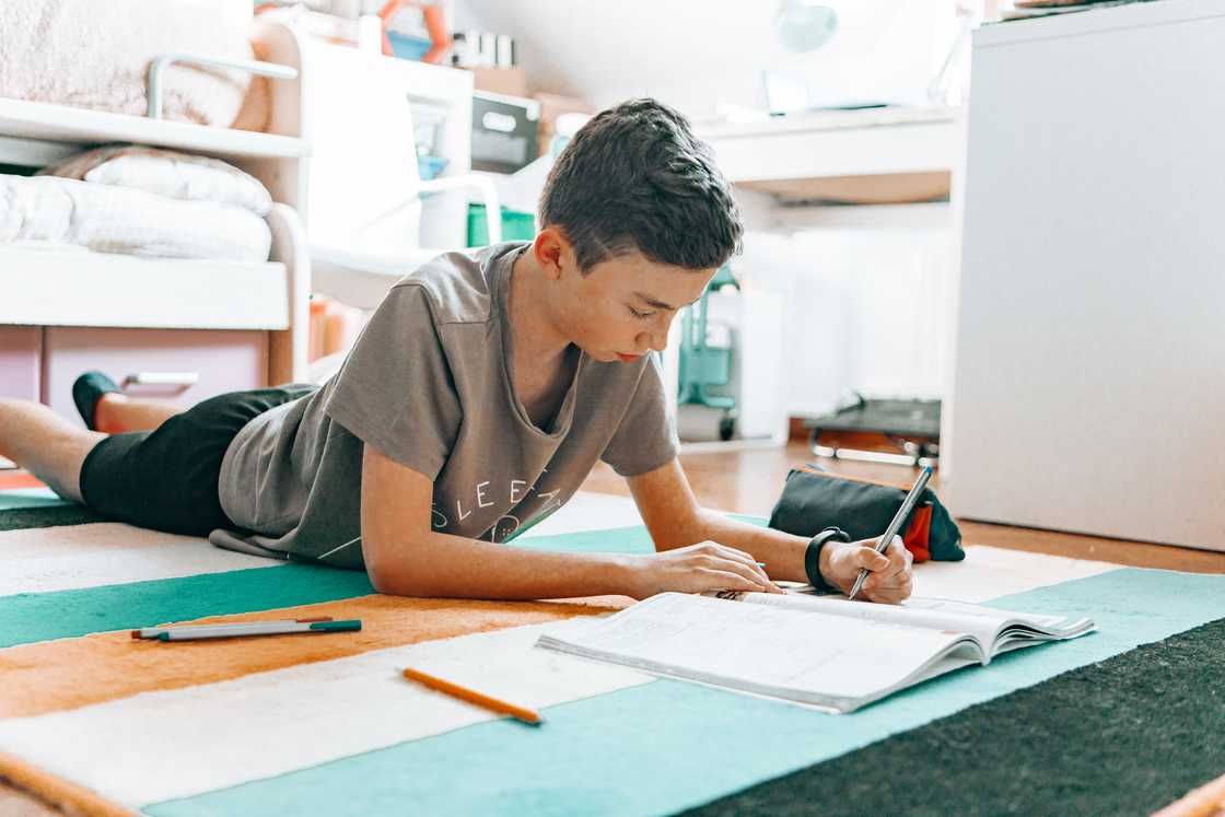A boy drawing while lying on the floor A boy drawing while lying on the floor