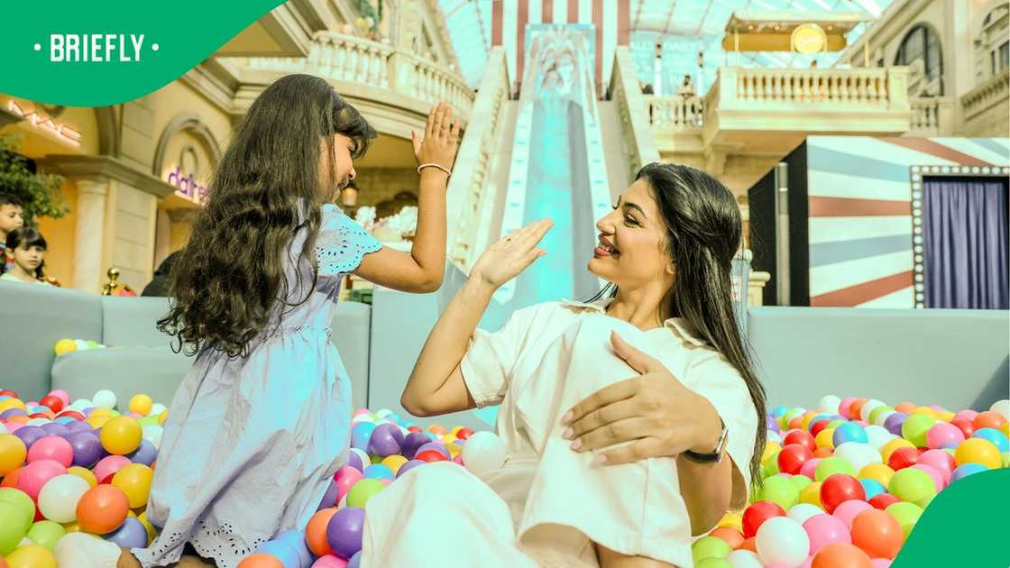 A woman and a young girl high-five each other while playing in a large indoor ball pit filled with vibrant, colorful plastic balls.