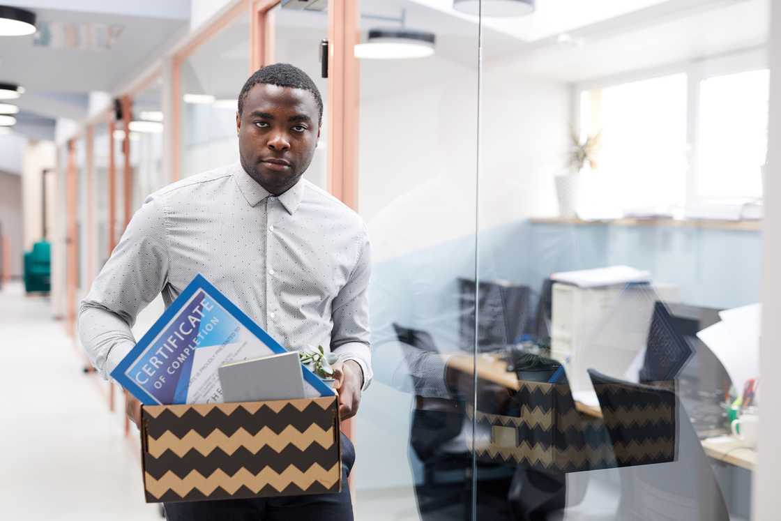 Person walks through an office hallway carrying a cardboard box filled with personal items. Person walks through an office hallway carrying a cardboard box filled with personal items.