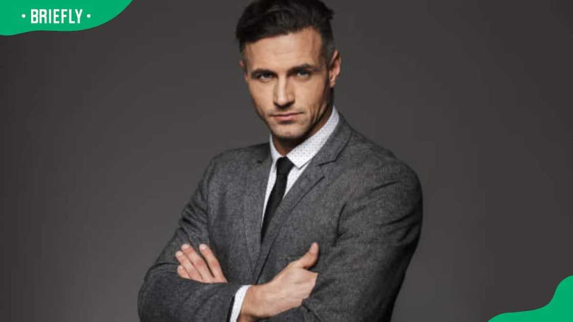 A masculine man wearing a charcoal grey business suit poses on camera A masculine man wearing a charcoal grey business suit poses on camera