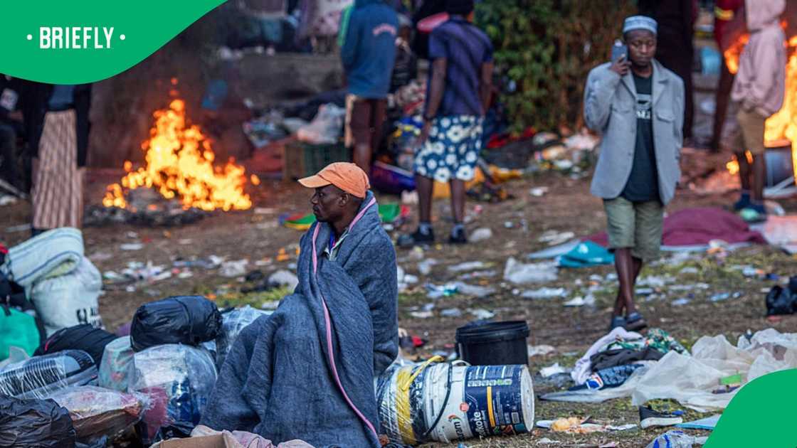 A man sits with a blanket to keep warm as thousands of Malawians take refuge on June 20, 2026 in Sherwood Park outside Durban, South Africa. Around 12,000 people have passed through the camp in recent weeks