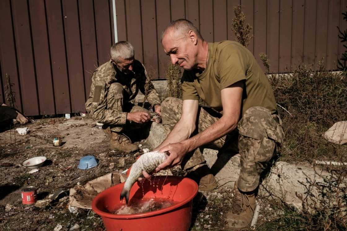 Ukrainian soldiers clean fish they have caught  for cooking, in the recently recaptured resort village of Shchurove