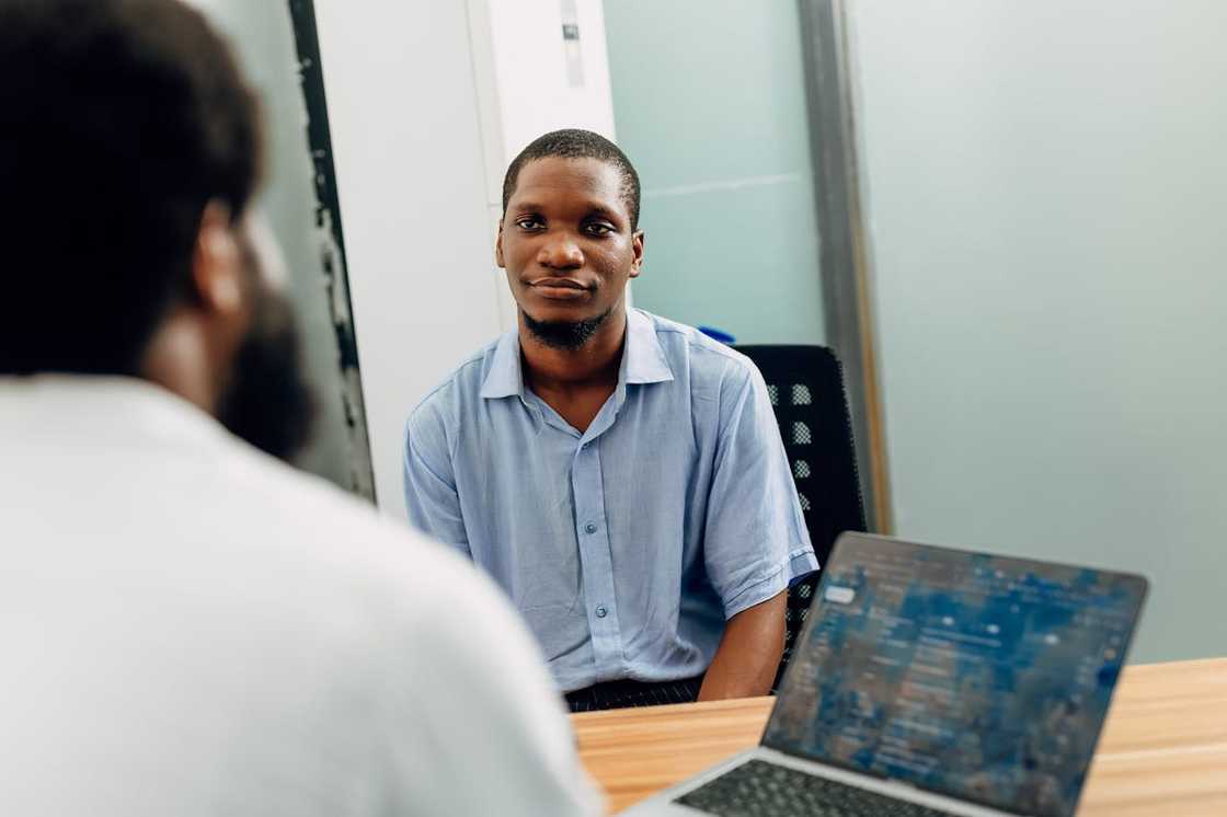 A man seated in a chair, listening attentively during an interview session. A man seated in a chair, listening attentively during an interview session.