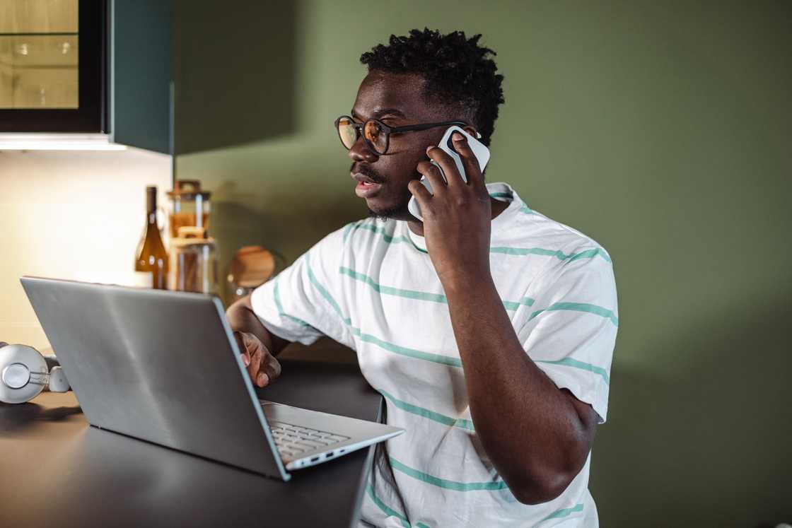 A young man using a laptop and talking on the phone.
