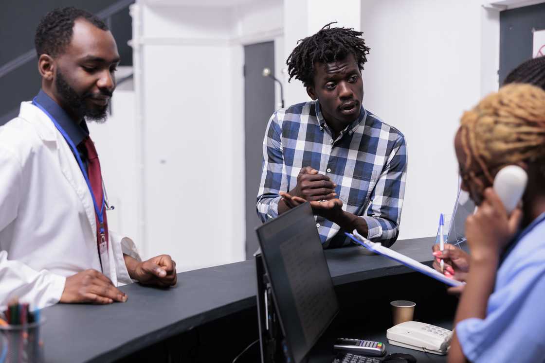 A man speaks anxiously with nurses at a station. A man speaks anxiously with nurses at a station.