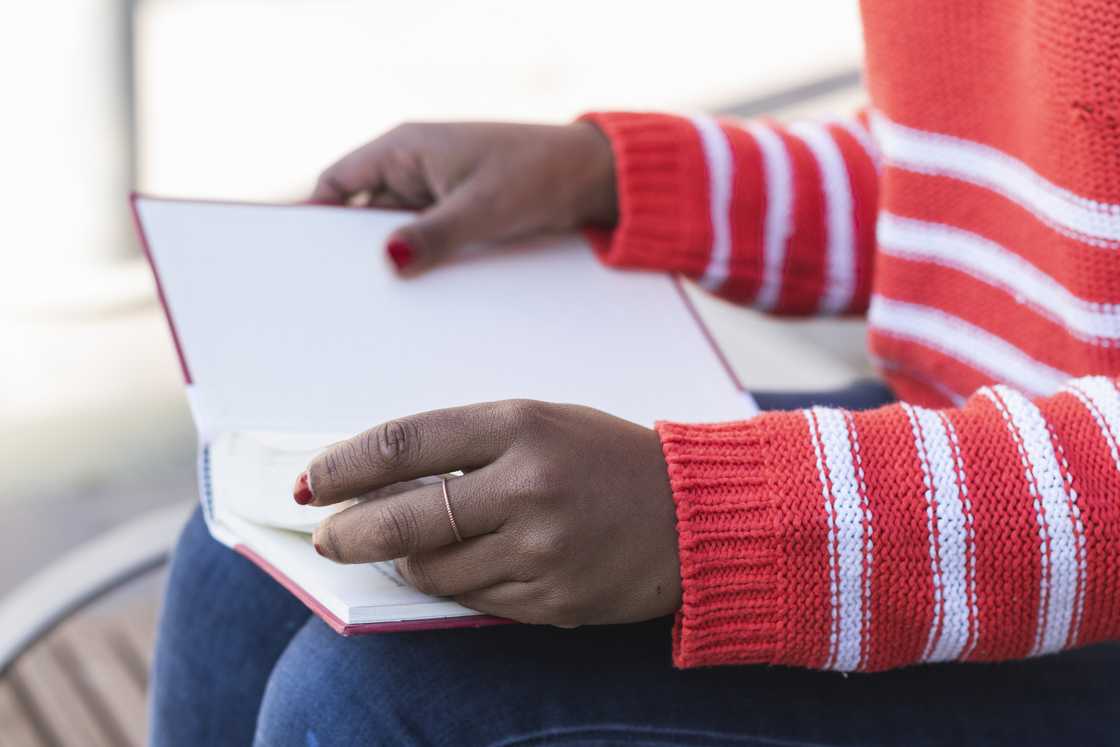 Person in a red and white striped sweater holds an open book. Person in a red and white striped sweater holds an open book.