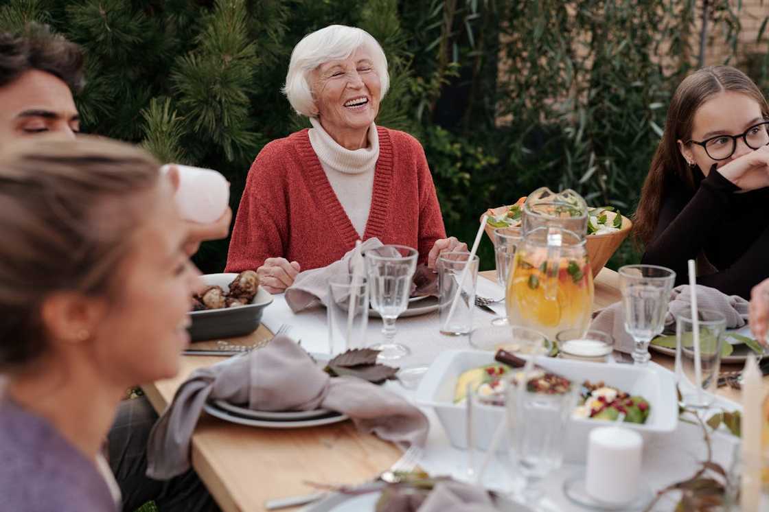 Elderly woman laughing while sharing a meal with family at an outdoor table. Elderly woman laughing while sharing a meal with family at an outdoor table.