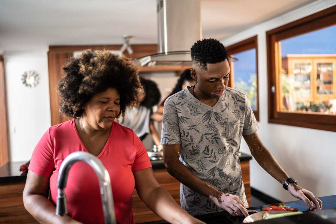 Two people in a kitchen, one at the sink and one at the stove.