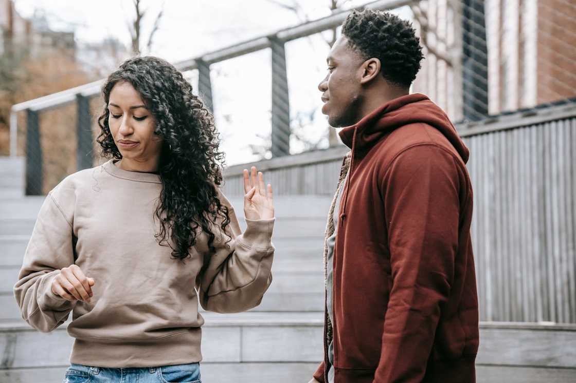 A woman raises her hand as she faces a man during a tense outdoor conversation.