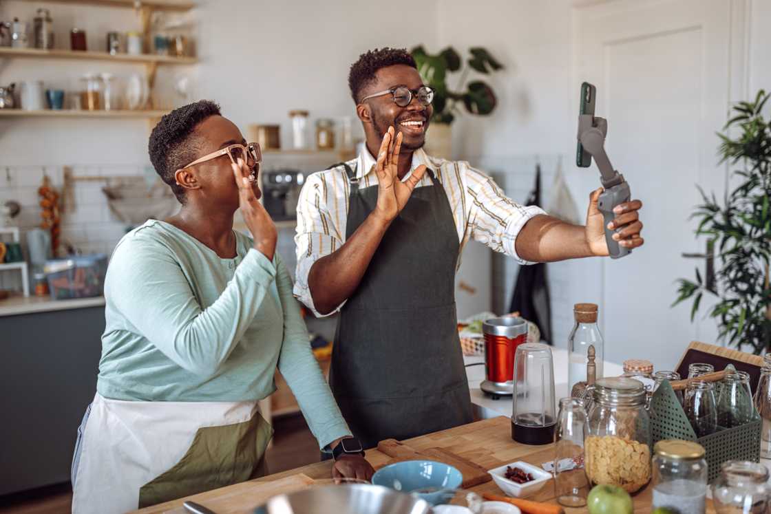 A couple laughs while filming a cooking video in their kitchen.