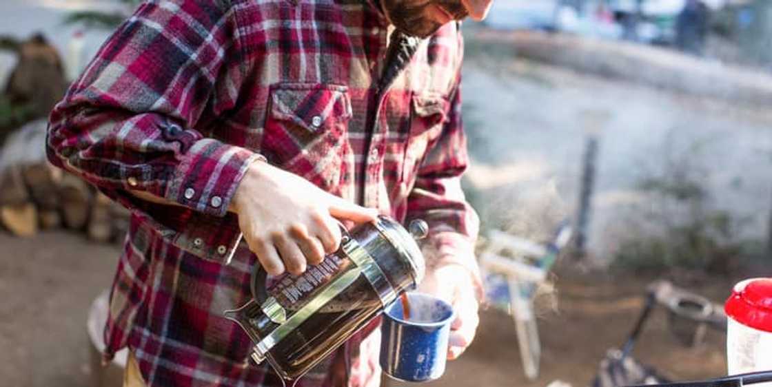 Man wearing a flannel shirt preparing coffee while camping Man wearing a flannel shirt preparing coffee while camping