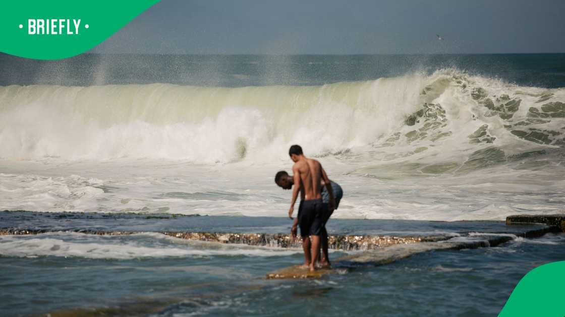 Two boys get ready to dive into a tidal pool as waves spray water by the seaside of Kalk Bay in Cape Town on September 17, 2023 following the spring high tide in the Western Cape province
