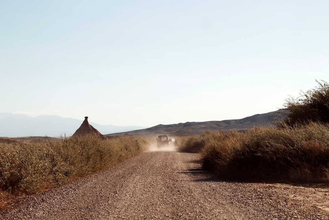 A car driving away on a dusty road